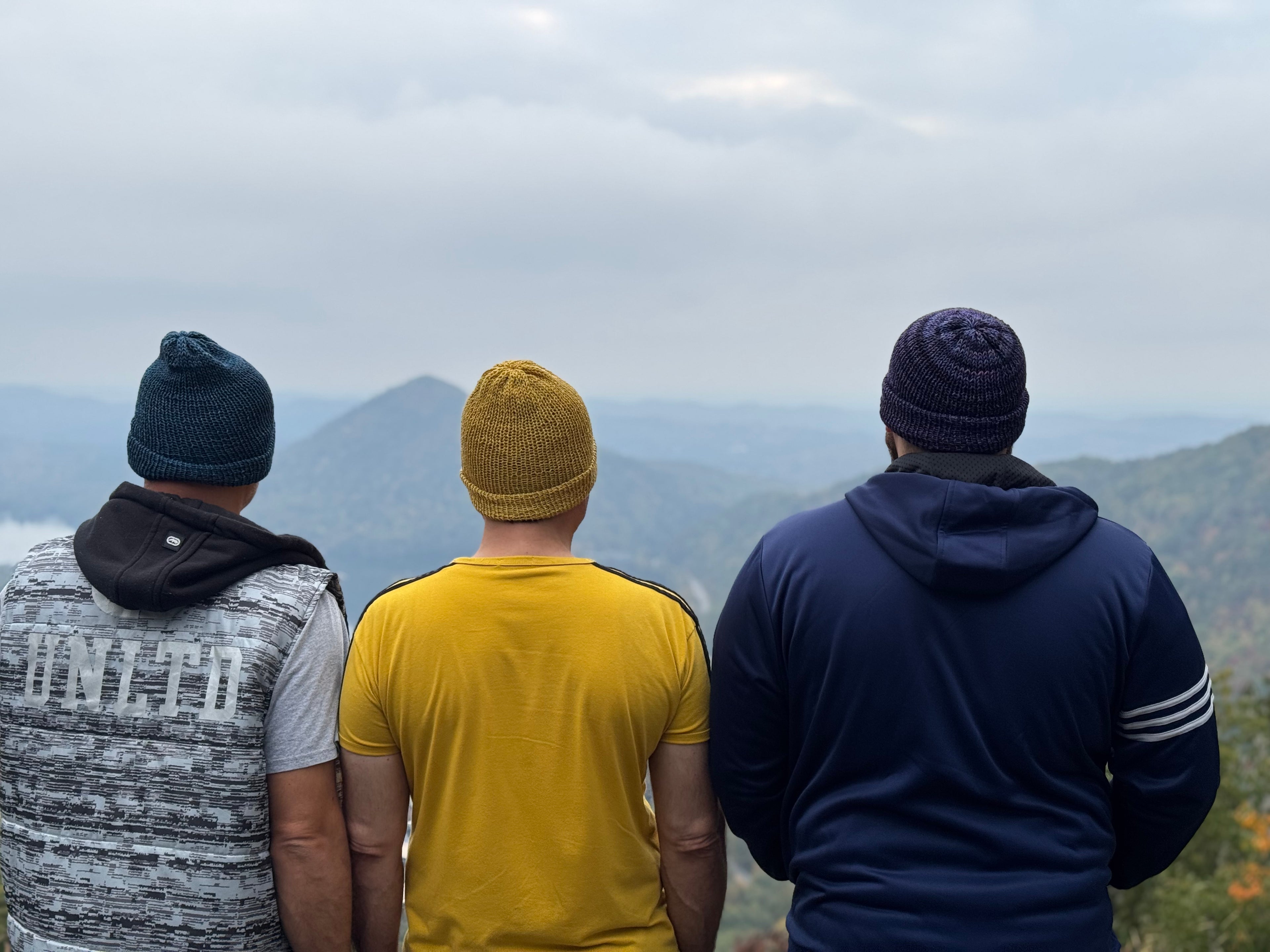 Knitty Gritty Witty Handmade hats are shown in this picture with 3 heads and a mountain background 